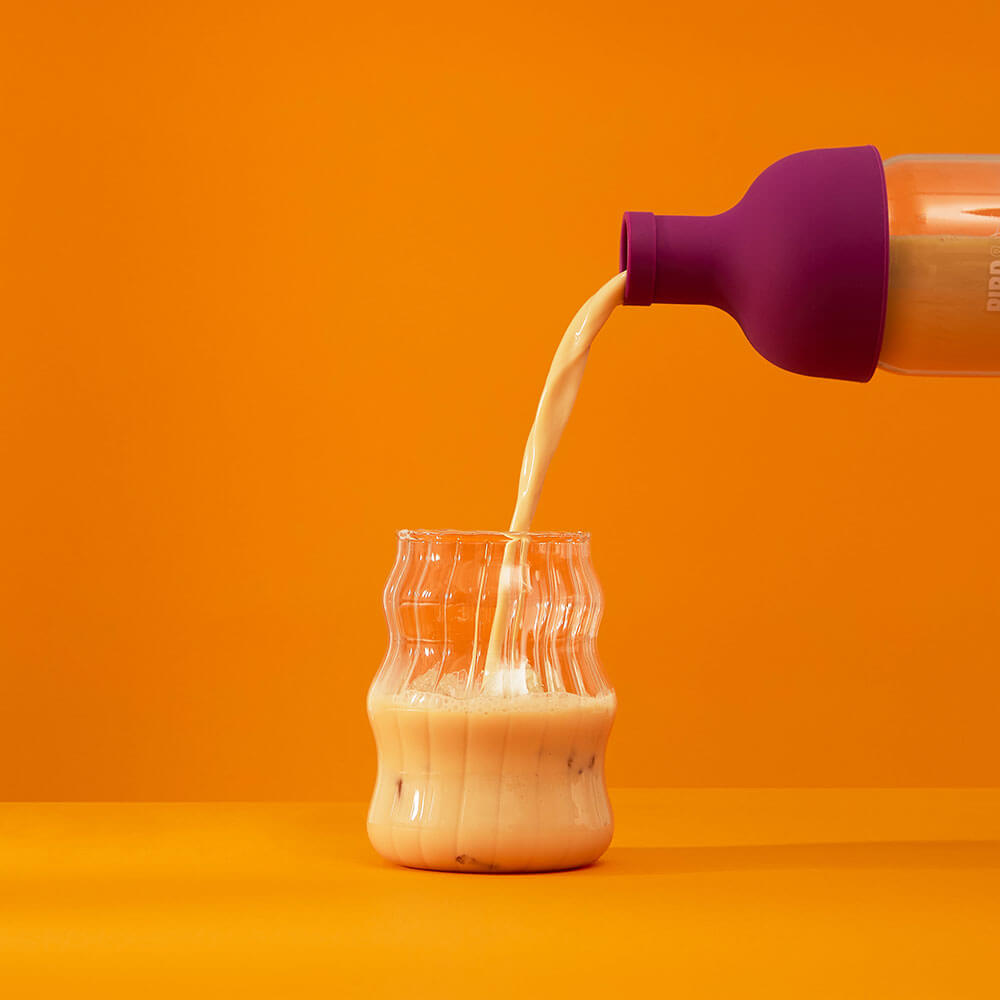 iced spiced pumpkin sticky chai pouring from a plum purple cold brew tea bottle into cup with ice