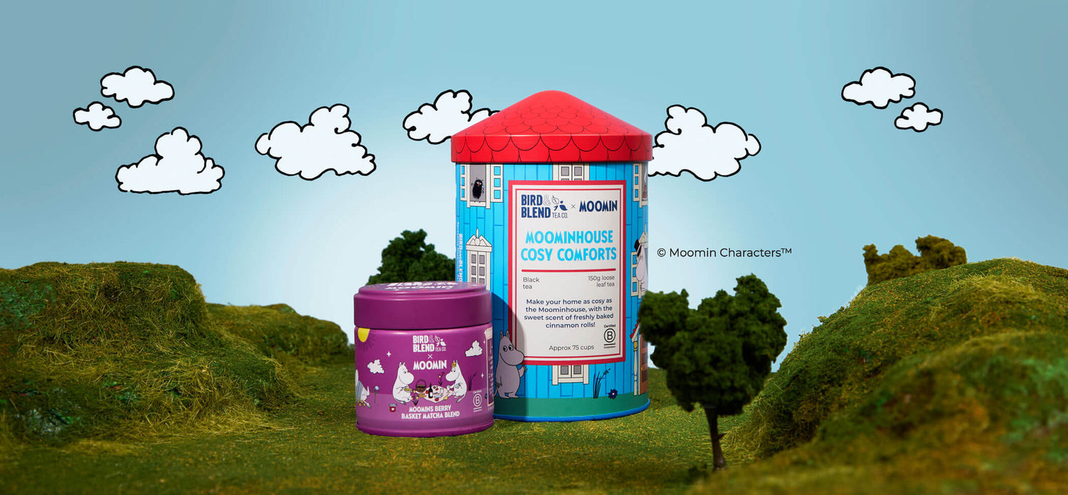 Moomins berry basket matcha tin & moomins cosy comforts tea tin on grass with a sky blue background &clouds