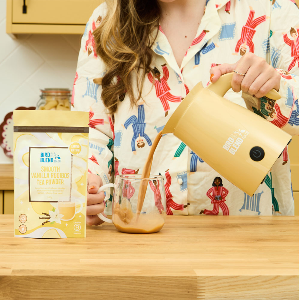 Smooth vanilla rooibos tea powder pouch &amp; person pouring hot smooth vanilla rooibos tea powder from a bamboo gloss matcha latte magic whisk into a mug
