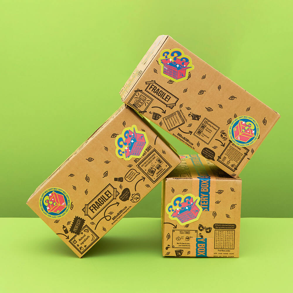 Three mystery tea boxes balanced on each other with a green background